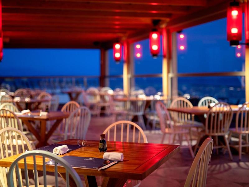 Večerní terasa restaurace s dřevěnými stoly a tlumeným červeným osvětlením.