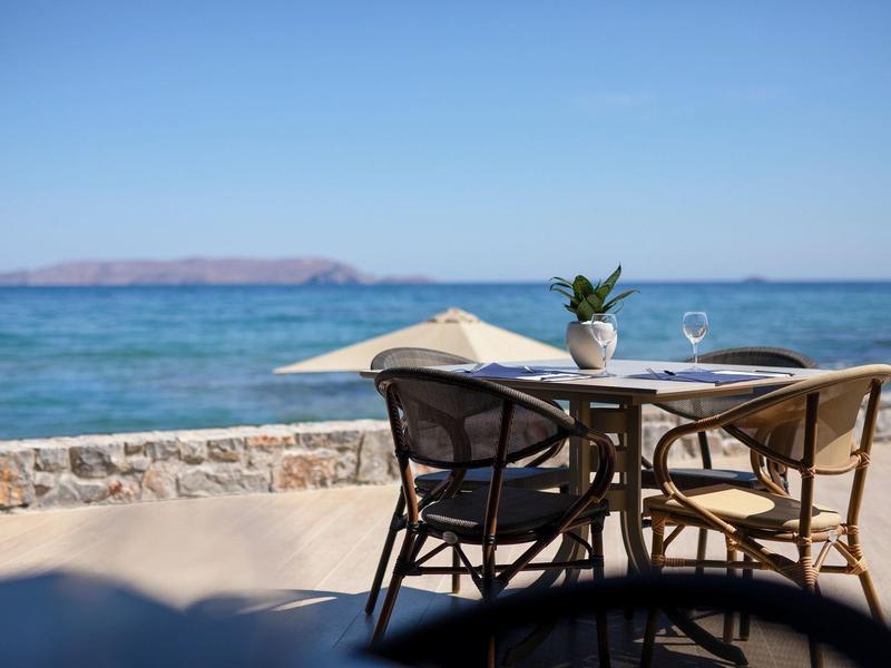 Ratanový stůl a židle s výhledem na moře pod jasnou oblohou.