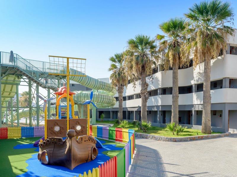 Barevné hřiště před moderní budovou s palmami za slunečného počasí.