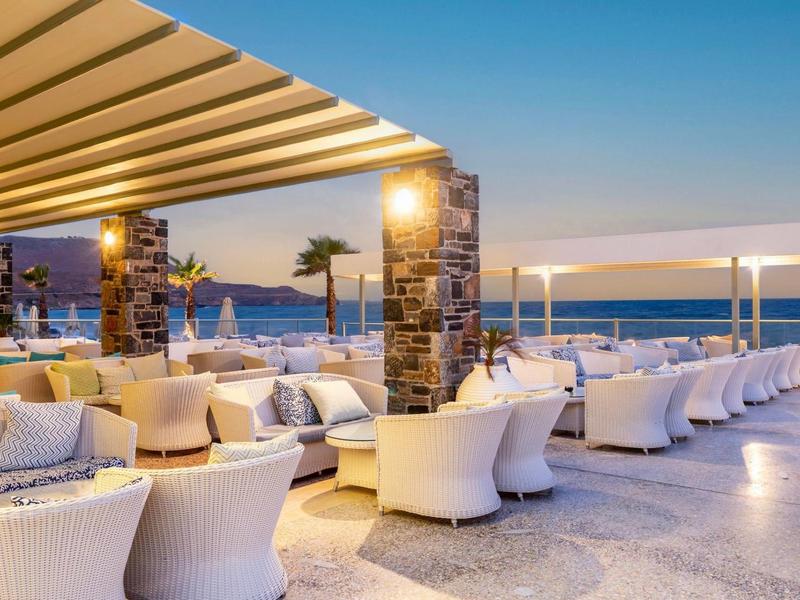 Elegantní venkovní restaurace s výhledem na moře za západu slunce.