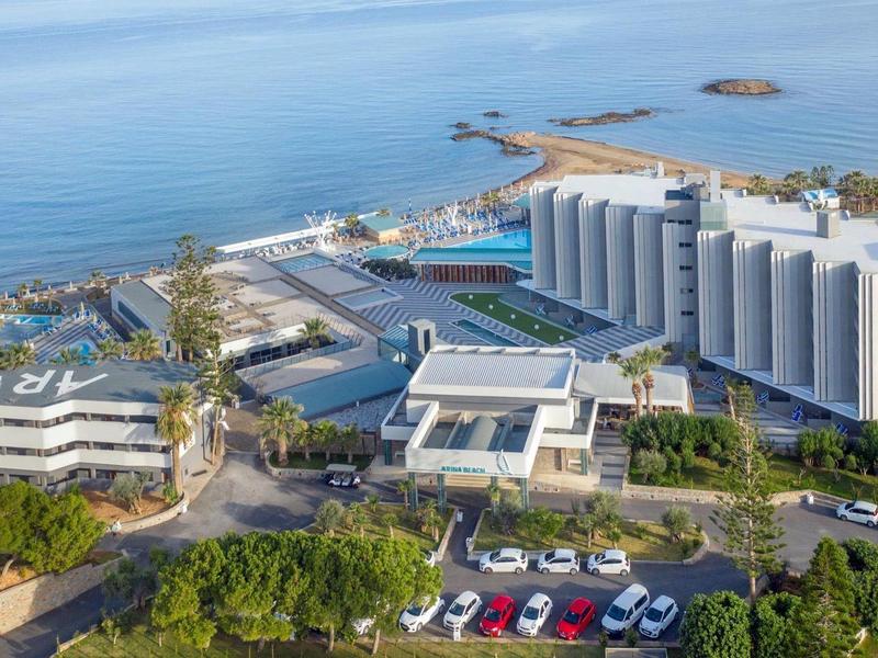 Letecký pohled na velký hotelový komplex u moře s bazénem a vegetací.