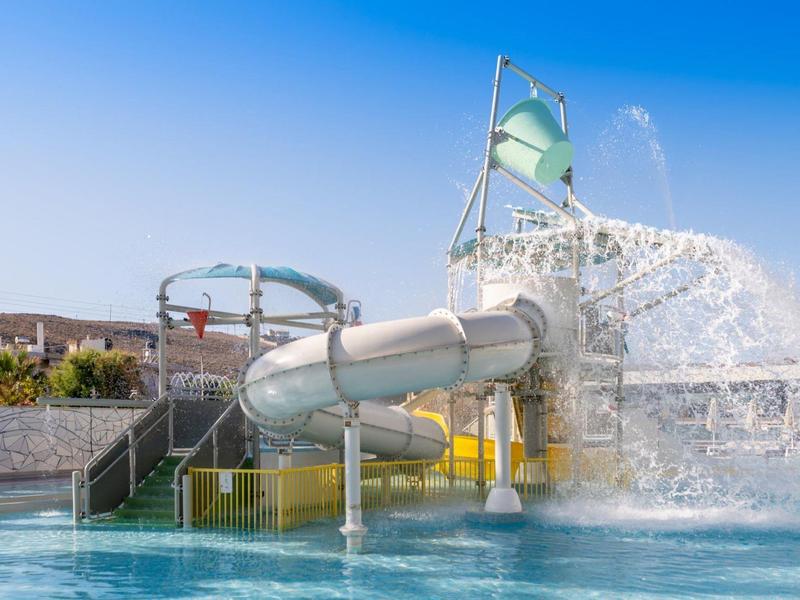 Vodní skluzavka s velkým vodopádem a bazénem pod modrou oblohou.