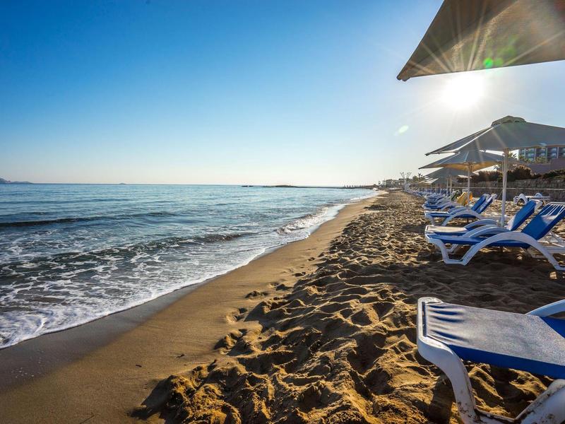 Písčitá pláž s lehátky a slunečníky pod jasně modrou oblohou.
