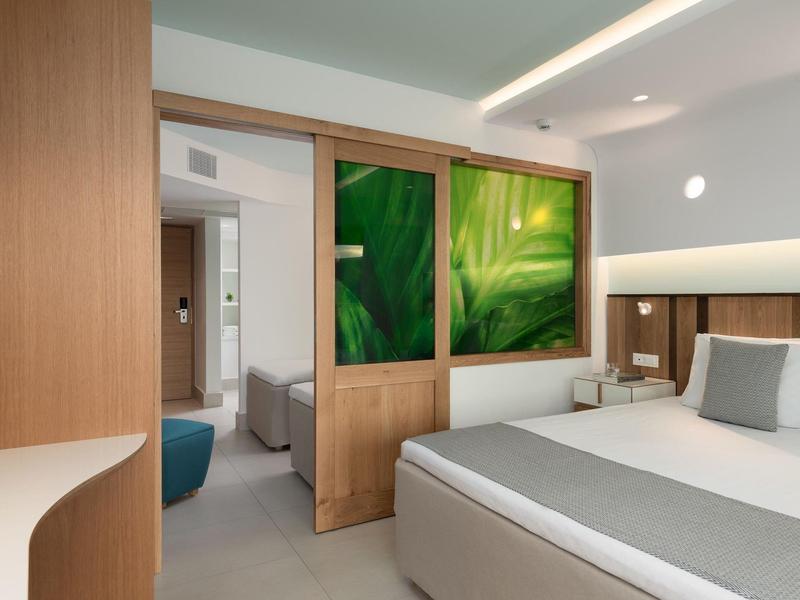 Moderní hotelový pokoj s dvoulůžkem a posuvnými dveřmi zdobenými zelenými listy.