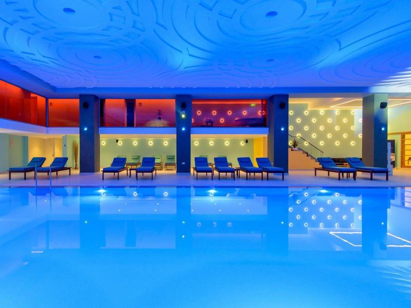 Moderní krytý bazén s modrým osvětlením a pohodlnými křesly.