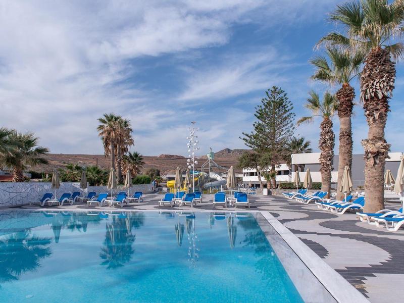 Modrý bazén obklopený lehátky a palmami pod částečně oblačnou oblohou.