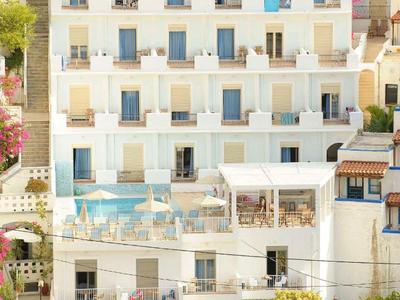 Wielopiętrowy hotel z balkonami, basenem i parkingiem otoczony drzewami.