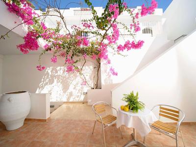 Patio luminoso con paredes blancas, flores rosas y zona de descanso con mesa y sillas.