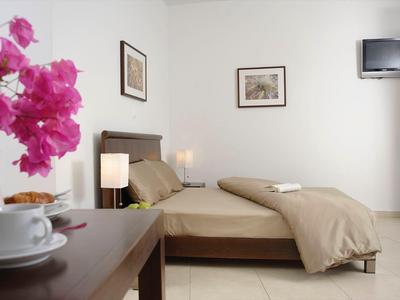 Przytulny pokój hotelowy z łóżkiem podwójnym, telewizorem i kwiatową dekoracją na stole.