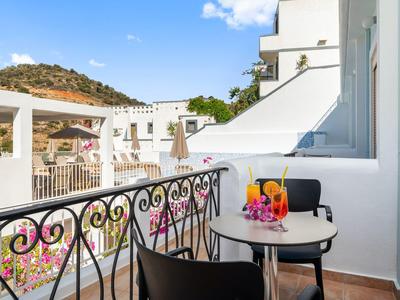 Balkon ze stolikiem i napojami, widok na białe budynki i wzgórza pod czystym niebem