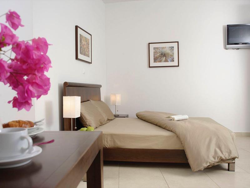 Przytulny pokój hotelowy z łóżkiem podwójnym, telewizorem i kwiatową dekoracją na stole.