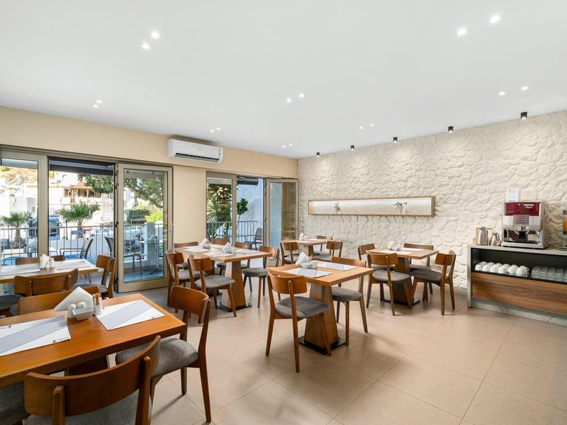 Jasna, nowoczesna restauracja z drewnianymi stołami i krzesłami, dużymi oknami i bufetem.