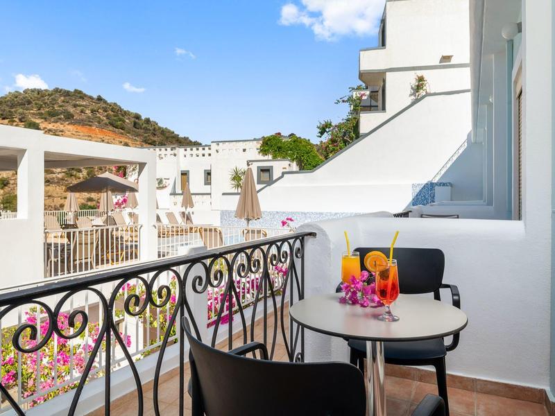 Balkon ze stolikiem i napojami, widok na białe budynki i wzgórza pod czystym niebem