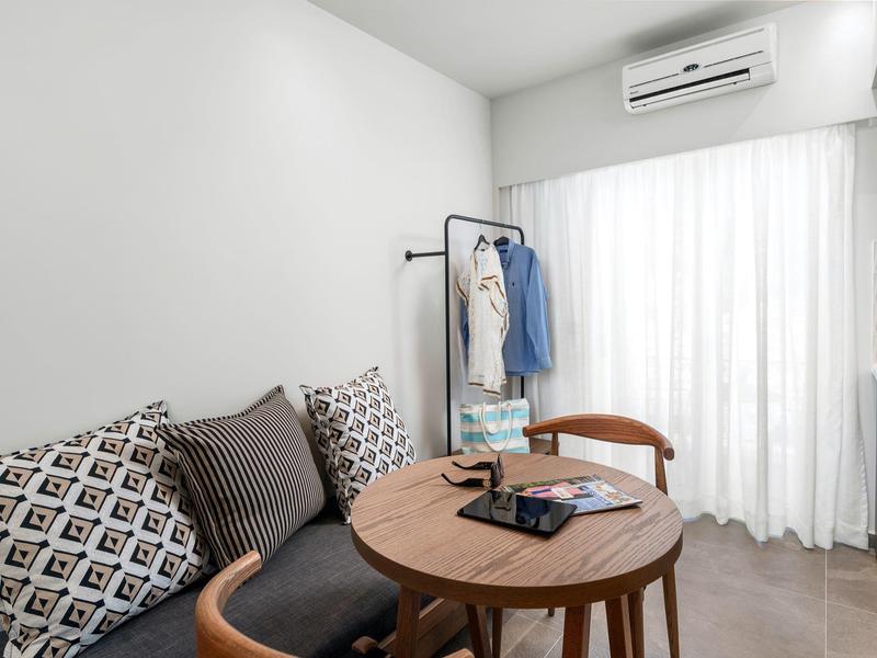 Nowoczesny obszar pokoju hotelowego z okrągłym drewnianym stołem, krzesłami i klimatyzatorem na ścianie.