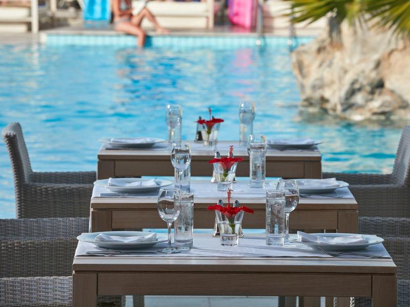 Étables de restauration au bord de la piscine avec tables, chaises, verrerie et piscine en arrière-plan.