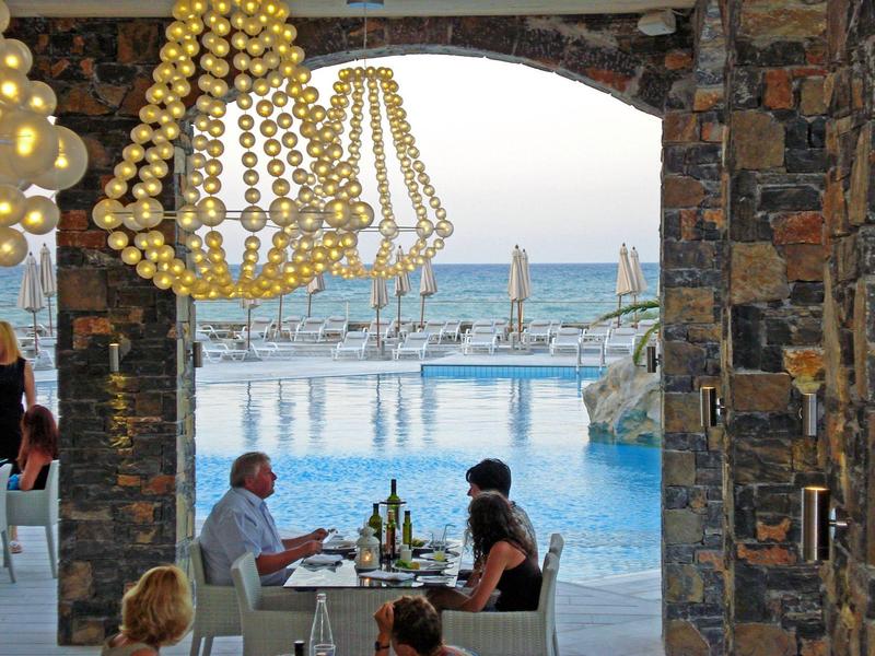Couple dîne à une table près d'une piscine avec vue sur l'océan à travers une arche en pierre.
