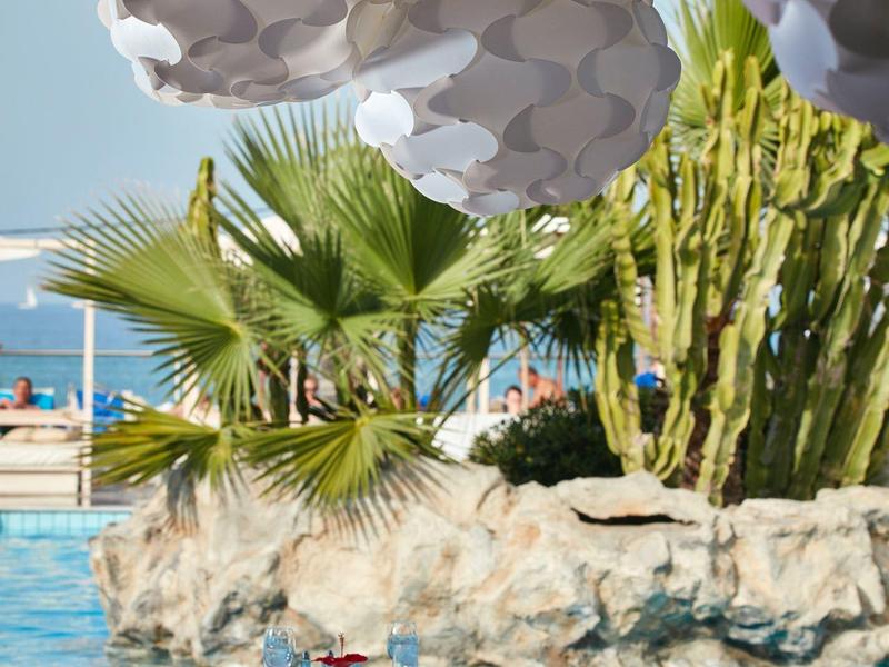 Espace repas extérieur au bord de la piscine avec lanternes blanches suspendues, palmiers et cactus en arrière-plan