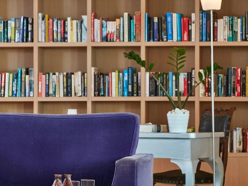 Coin lecture confortable avec un canapé bleu, une table en verre, une lampe sur pied et une grande bibliothèque en bois.