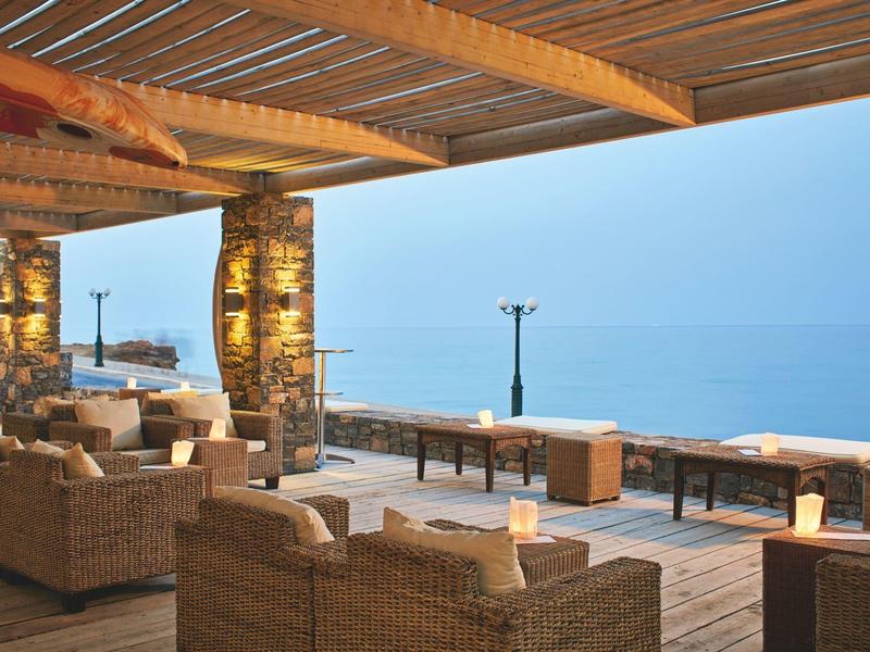 Coin salon extérieur confortable avec mobilier en osier et vue sur la mer au crépuscule.