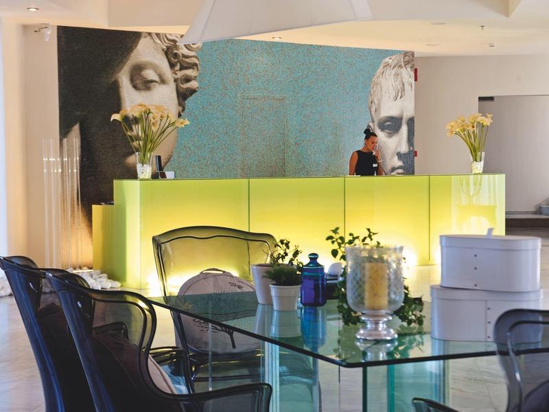 Intérieur moderne avec table en verre, chaises noires et grands portraits artistiques sur mur vert citron.
