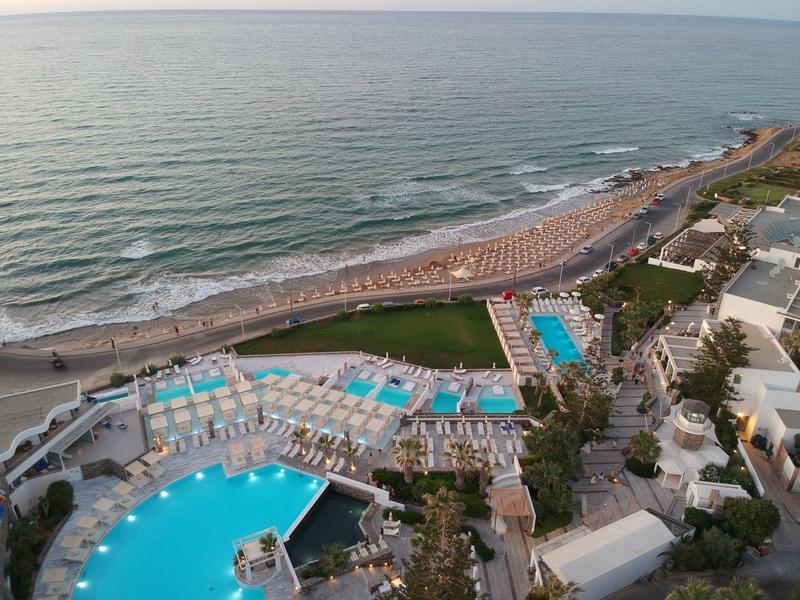 Vue aérienne d'une station balnéaire avec grandes piscines et chaises longues au bord de la mer.