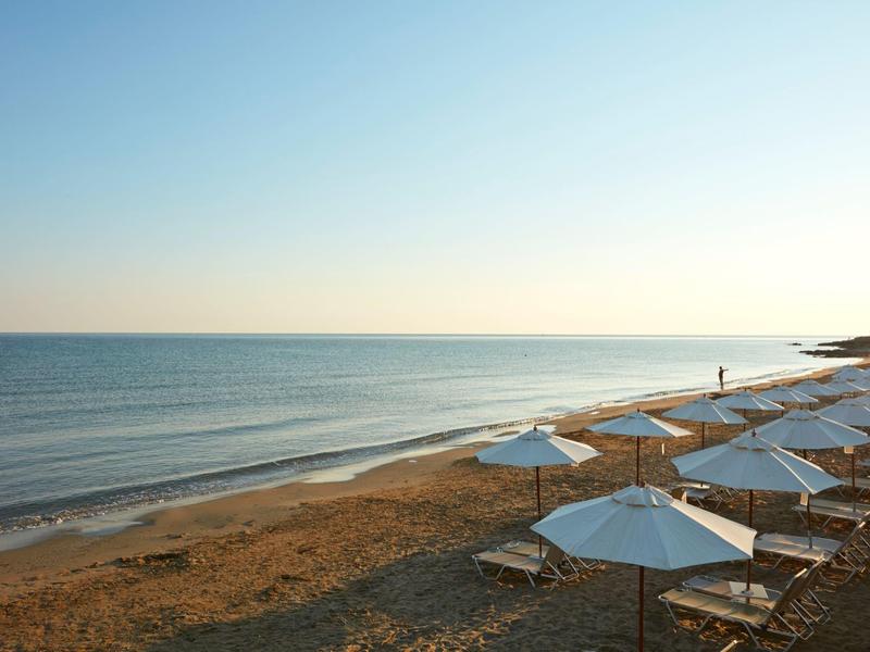 Plage calme avec rangées de parasols blancs et chaises longues sous un ciel clair.