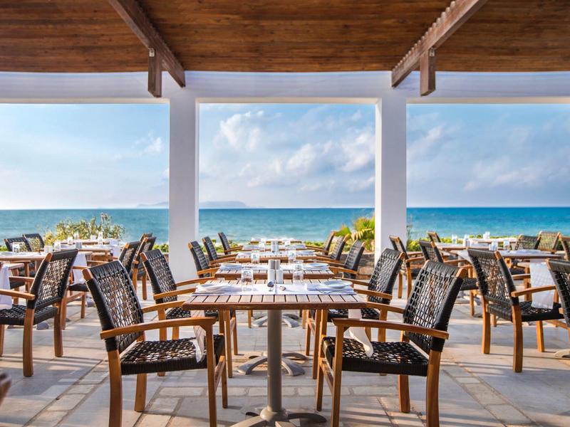 Terrasse de restaurant avec chaises et tables en bois face à la mer et ciel bleu.