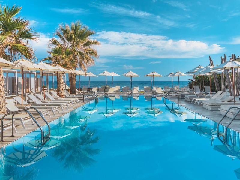 Piscine extérieure avec chaises longues et parasols sous un ciel bleu dans un complexe tropical.