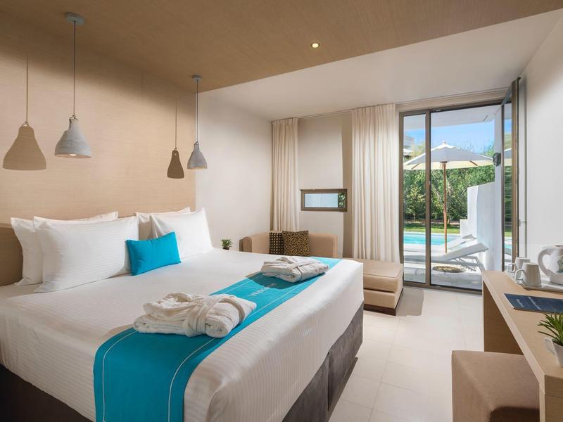 Chambre d'hôtel lumineuse avec grand lit, accents turquoise et porte vitrée ouvrant sur patio.