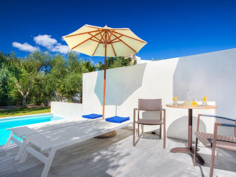 Espace au bord de la piscine ensoleillé avec chaises longues, parasol et table avec boissons.