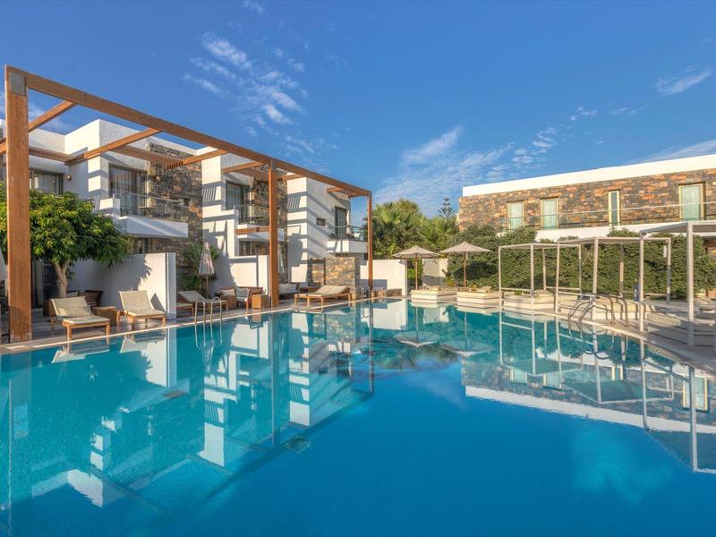 Hôtel moderne avec piscine extérieure, pergolas en bois et ciel clair ensoleillé.