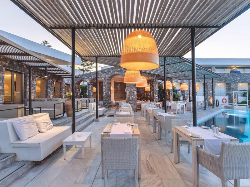 Espace lounge et repas extérieur moderne près d'une piscine au coucher du soleil avec éclairage chaleureux.