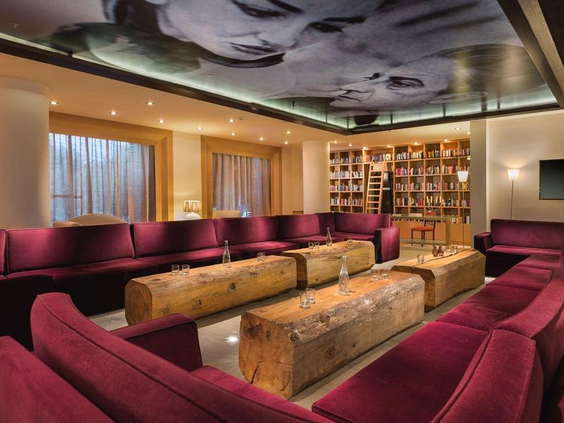 Salon chaleureux avec canapés bordeaux et tables en blocs de bois sous un éclairage artistique au plafond.