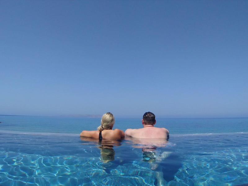 Couple profitant d'une piscine à débordement avec vue sur l'océan par une journée claire.