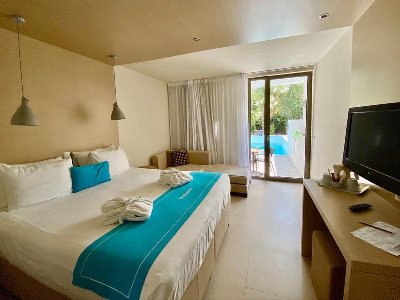 Chambre d'hôtel confortable avec lit double, accents turquoise, TV et balcon donnant sur la piscine.