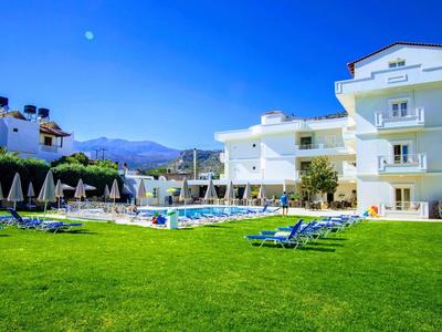 Hotel s velkým zeleným trávníkem, lehátky a bazénem za slunečného dne.