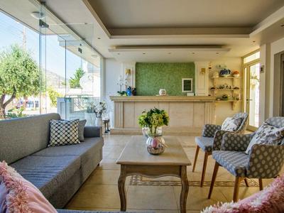 Jasny salon hotelowy z dużymi oknami, sofą, fotelami i recepcją w tle.