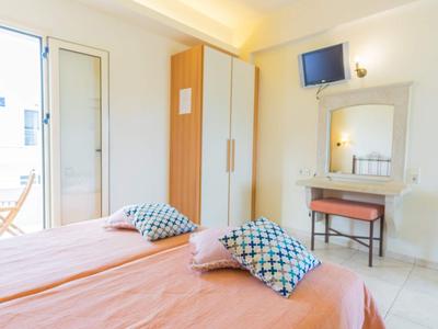 Světý hotelový pokoj se dvěma postelemi, barevnými polštáři, malým stolem a balkonem.