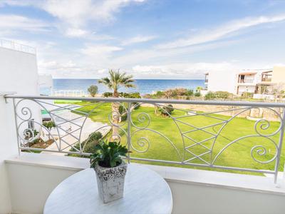 Balkon z metalową balustradą, stół z rośliną, widok na trawnik i morze w tle.