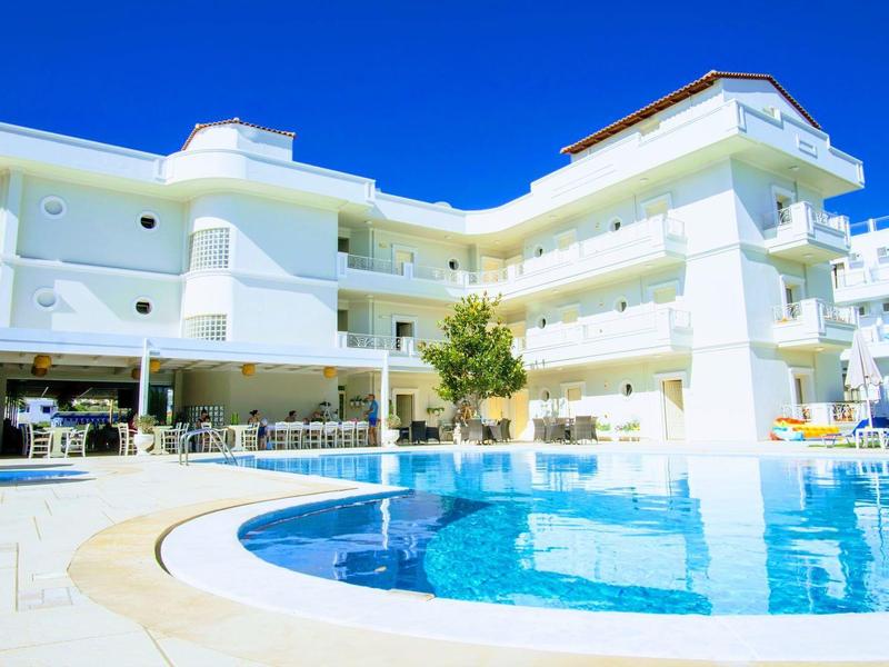 Bílý hotel s velkým kulatým bazénem a slunečníky venku.