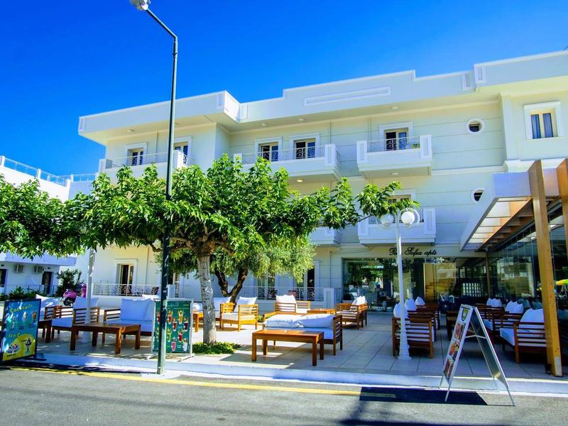 Hotel s venkovním posezením, zelenými stromy a jasnou modrou oblohou