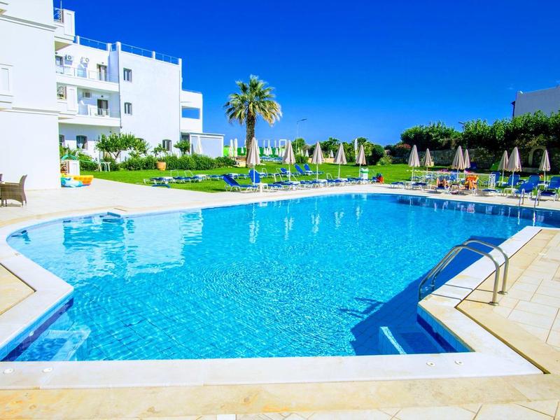 Moderní hotelový bazén s lehátky a zelenou krajinou pod jasně modrou oblohou.