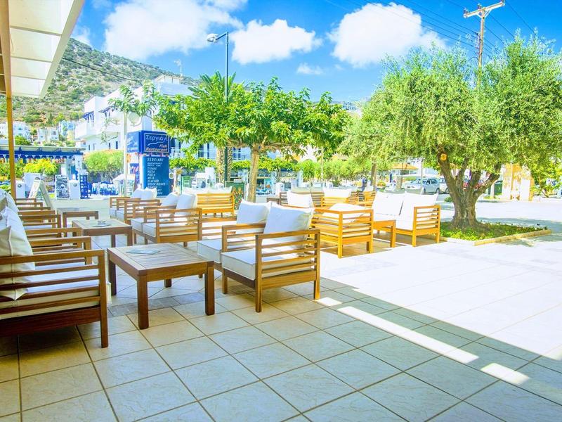 Venkovní prostor hotelu s dřevěným nábytkem, slunečníky a výhledem na zelené palmy.