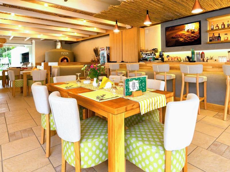 Světla moderní restaurace s dřevěným stropem, barem a stoly s bílými židlemi.