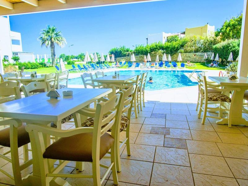 Venkovní hotelová jídelní část se stoly a židlemi vedle bazénu pod slunečníkem.