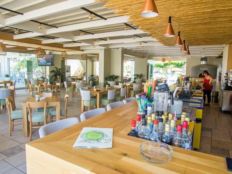 Světle zařízená restaurace s dřevěným nábytkem a dlouhým barem s nápoji.