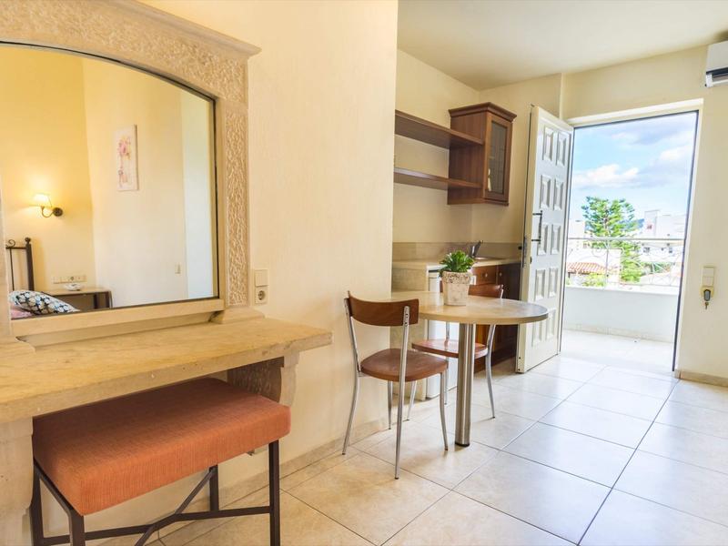 Pokoj s dřevěným nábytkem, stolem a židlemi, otevřené dveře na balkon nebo terasu