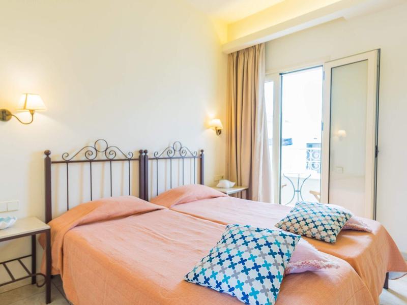 Světlo zařízená ložnice se dvěma samostatnými postelemi, oranžovými přikrývkami a balkónem s posuvnými skleněnými dveřmi.