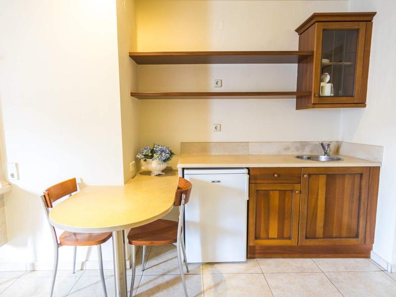 Malý kuchyňský kout s dřevěnými skříňkami, stolem, dvěma židlemi a mini lednicí.