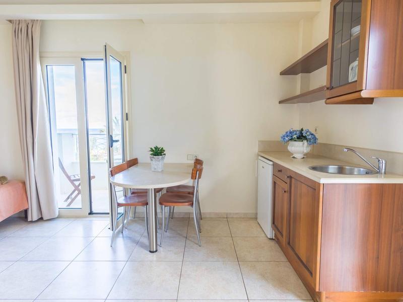 Světelná kuchyně s dřevěnými skříňkami, malým jídelním stolem se dvěma židlemi a přístupem na balkon.